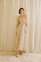 Woman in a floral dress with side cut-outs standing against a beige curtain backdrop