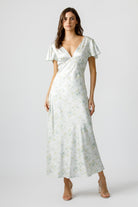 A woman wearing a soft pastel floral print maxi dress with a plunging V-neckline and fluttery short sleeves.