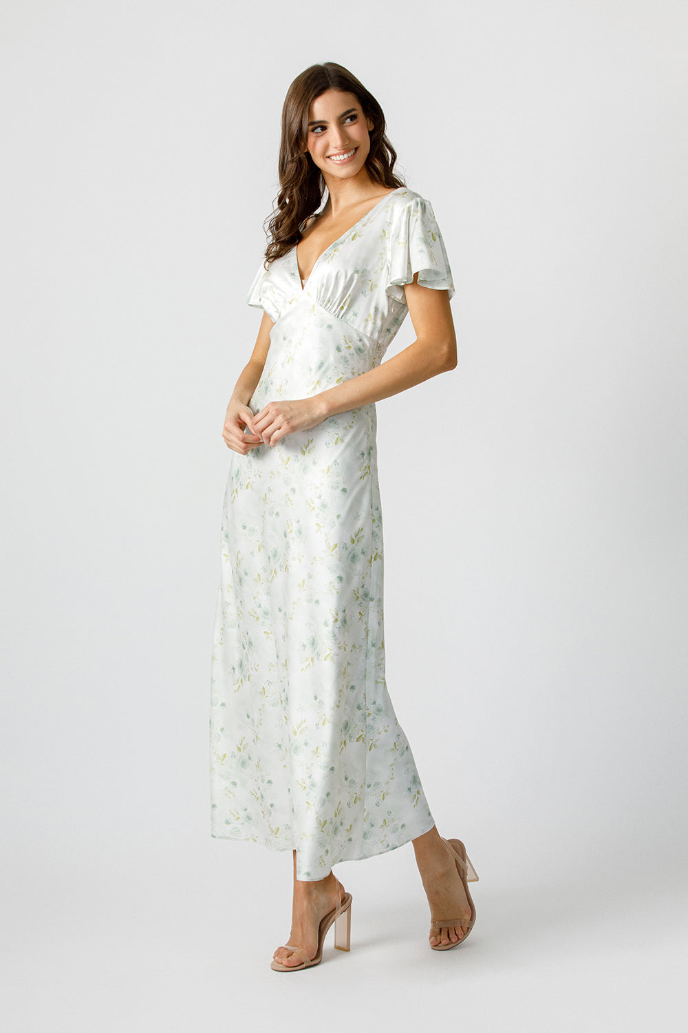 Side view of a woman wearing a soft pastel floral print maxi dress with a plunging V-neckline and fluttery short sleeves.