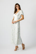 Side view of a woman wearing a soft pastel floral print maxi dress with a plunging V-neckline and fluttery short sleeves.