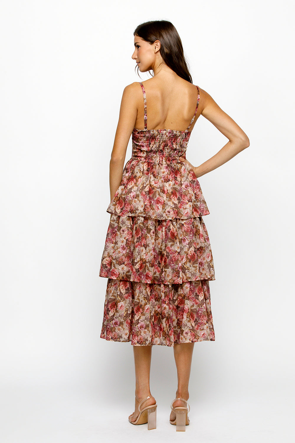Back view of a woman wearing a floral tiered dress on a white background