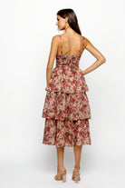 Back view of a woman wearing a floral tiered dress on a white background