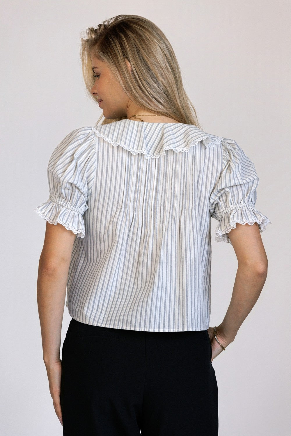 Back view of a woman wearing a striped blouse with ruffled sleeves against a plain background