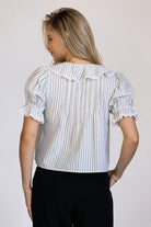 Back view of a woman wearing a striped blouse with ruffled sleeves against a plain background