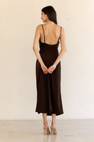 Back view of a woman wearing a brown slip dress against a white background