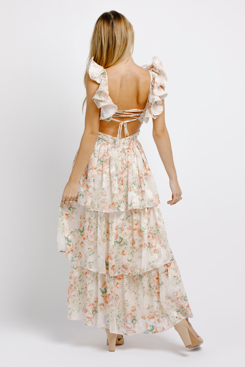 Back view of a woman wearing a cream floral maxi dress with ruffled sleeves on a white background