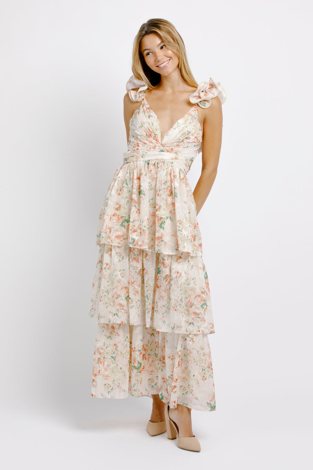 Woman wearing a cream floral maxi dress and beige heels on a white background