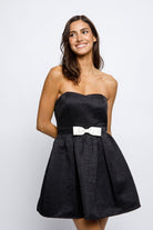 Woman wearing a black strapless dress with a white bow on a white background