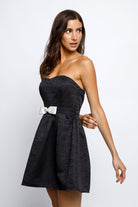 Woman wearing a black strapless dress with a white belt against a white background