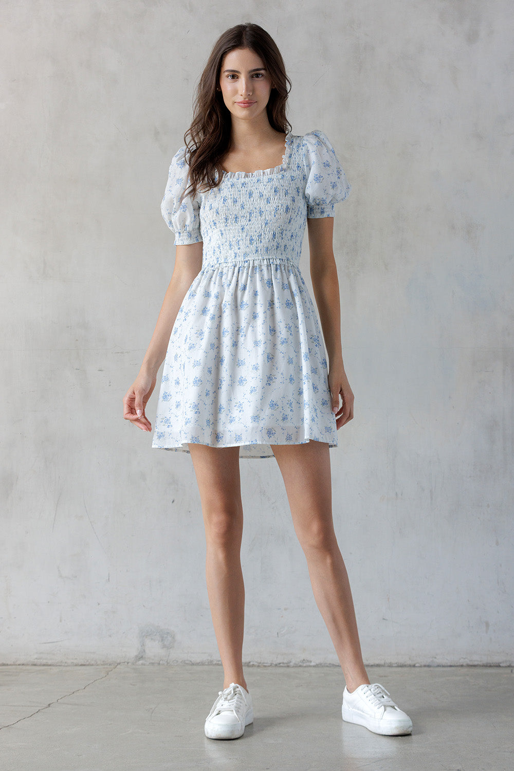 A woman modeling a blue floral mini dress and white sneakers.