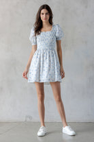 A woman modeling a blue floral mini dress and white sneakers.