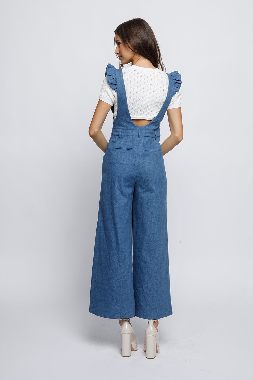 Woman wearing blue denim overalls and a white cropped top on a plain background