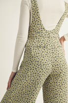 Person wearing a green floral jumpsuit and a white long sleeve top with a plain background