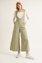 Woman wearing a green floral jumpsuit with a white top underneath on a plain background