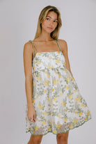 Woman wearing a floral dress with yellow flowers on a plain background