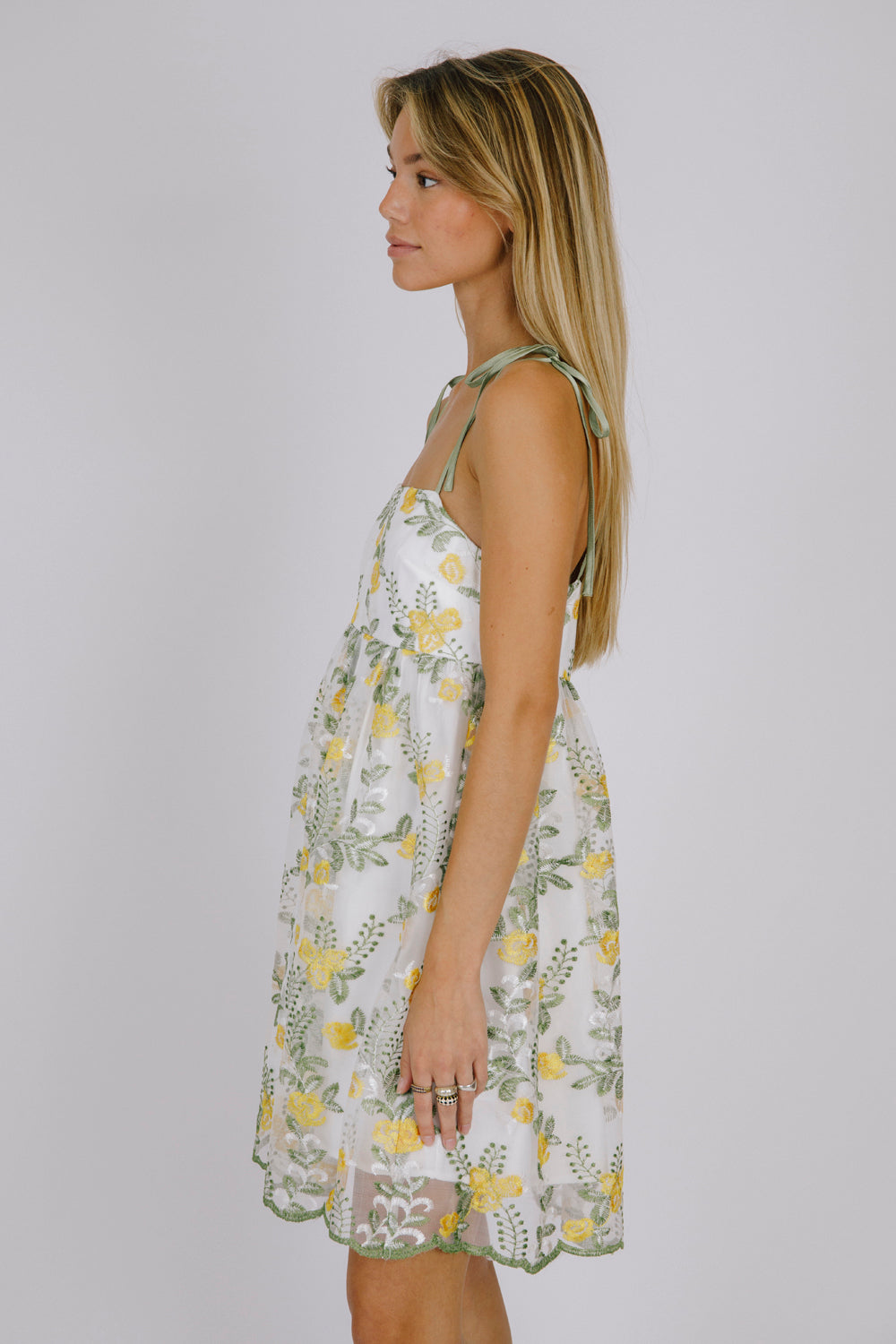 Side view of a woman wearing a floral dress with yellow flowers on a plain background