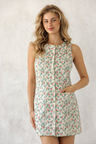 Model wearing a a vintage floral print, sleeveless shift silhouette, button-down front, and pockets for an effortlessly charming everyday look.