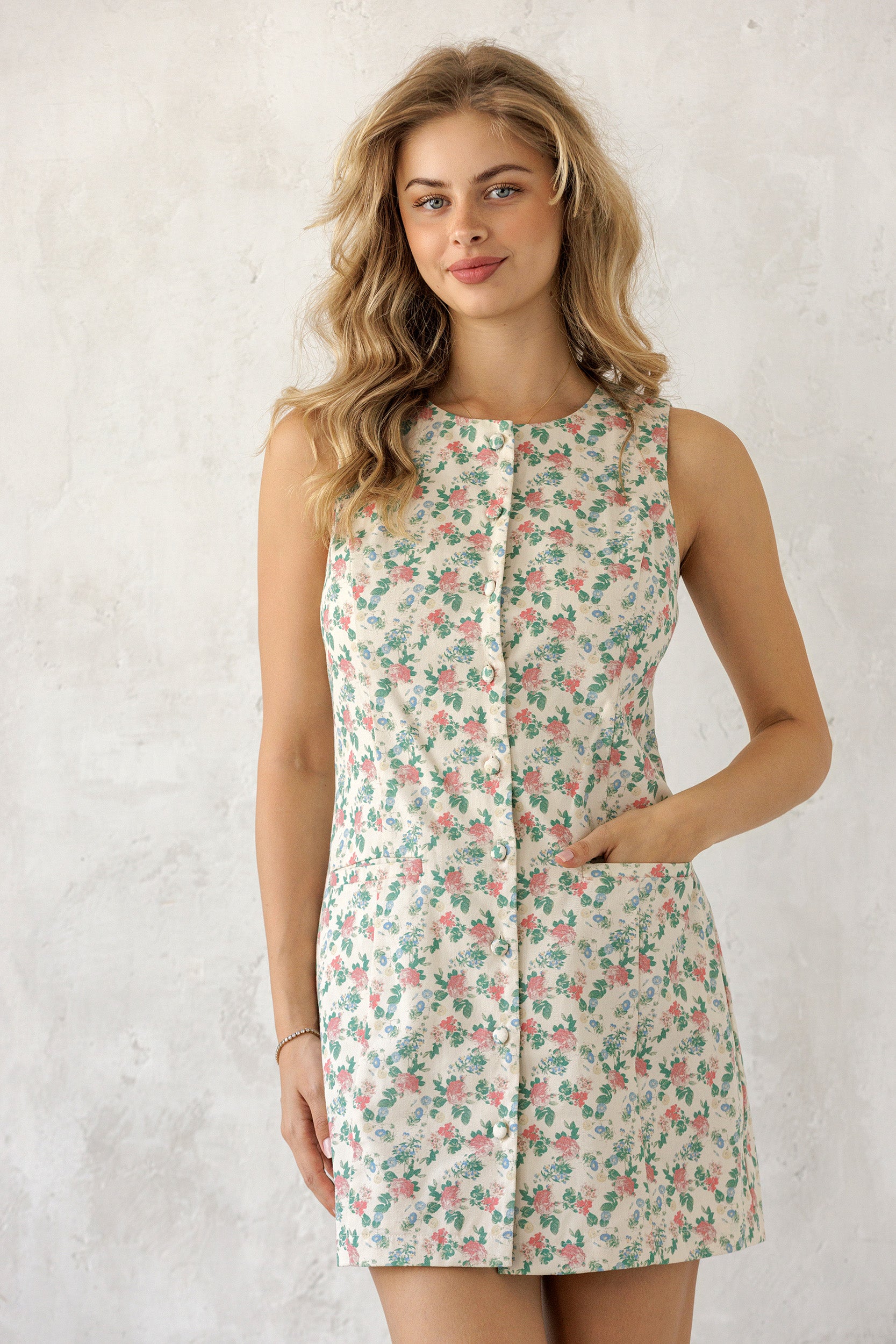 Model wearing a a vintage floral print, sleeveless shift silhouette, button-down front, and pockets for an effortlessly charming everyday look.