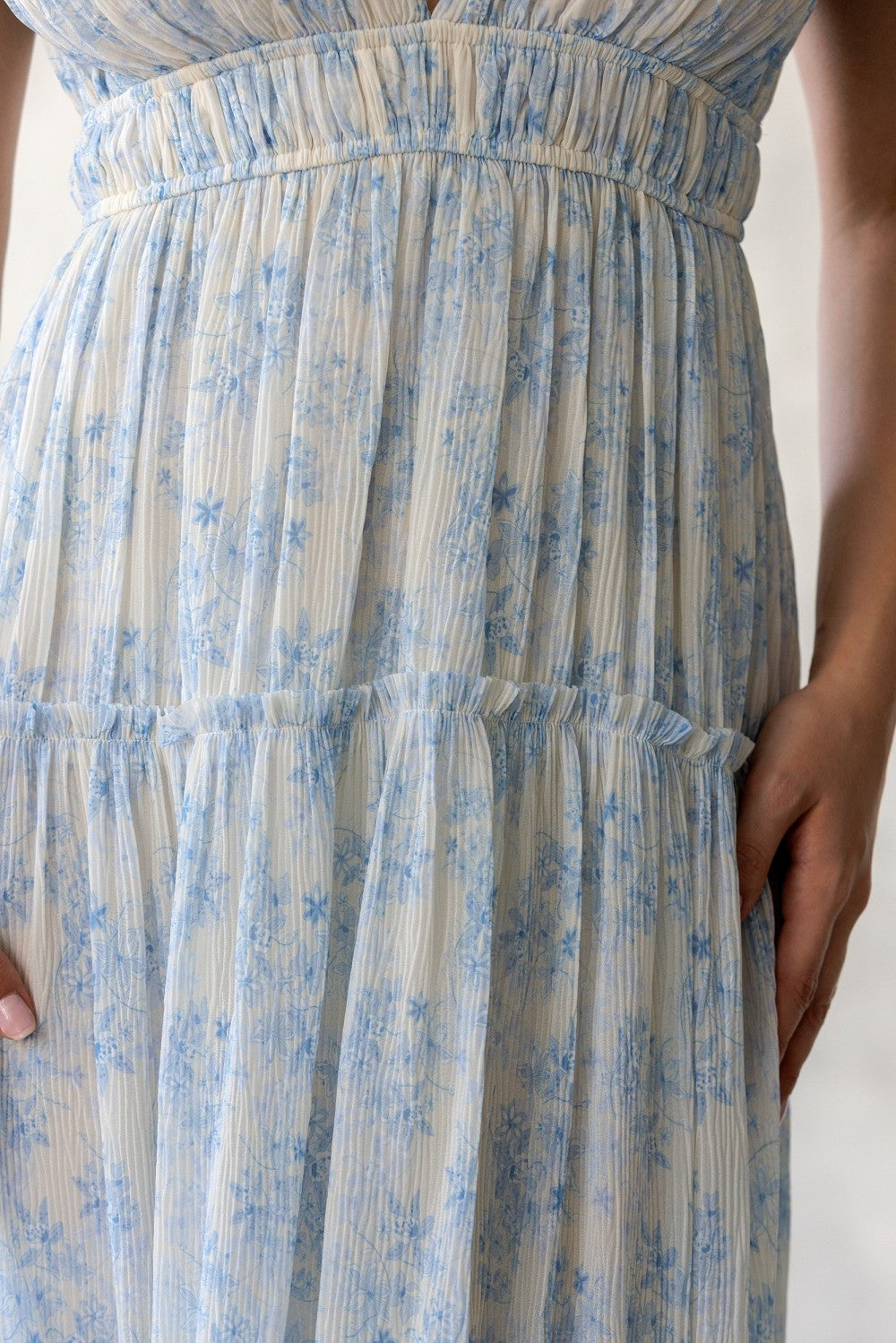 Close-up of a light-colored dress with blue floral pattern on a plain background