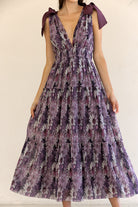 Woman wearing a purple floral dress with bow straps against a plain background