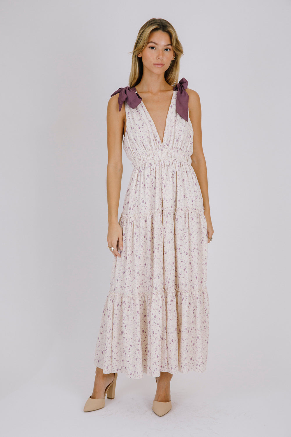 Woman wearing a purple floral maxi dress with bow straps details on a white background