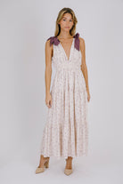 Woman wearing a purple floral maxi dress with bow straps details on a white background