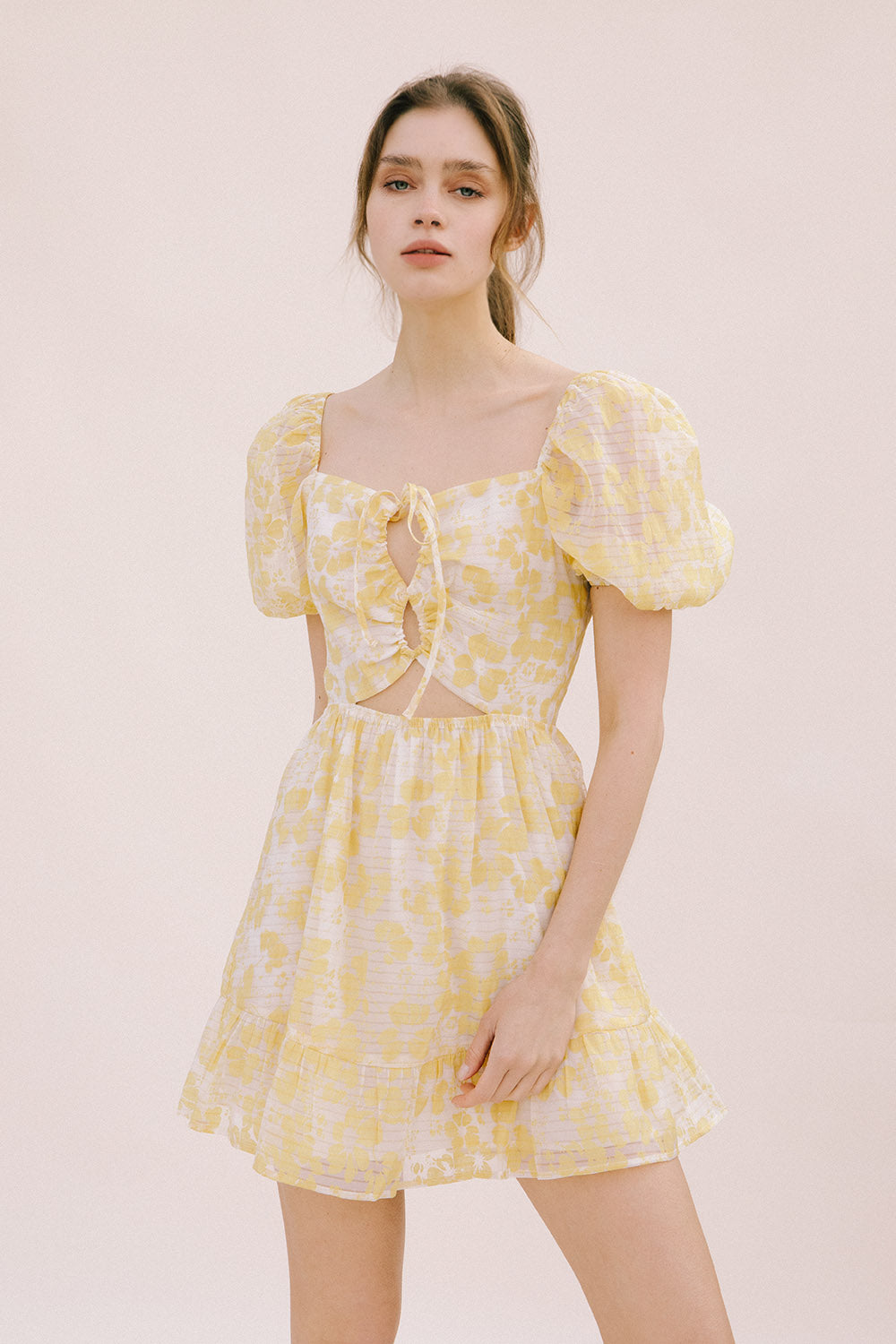 Woman wearing a yellow floral mini dress on a light pink background