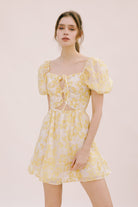 Woman wearing a yellow floral mini dress on a light pink background