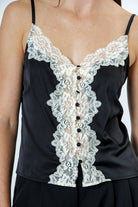 A person wearing a black top with floral lace trim, a v-neckline, adjustable spaghetti straps, and vintage-inspired button-front details.