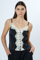 A model wearing a black top that features floral lace trim, V-neck silhouette, and vintage-inspired button details against a white background.
