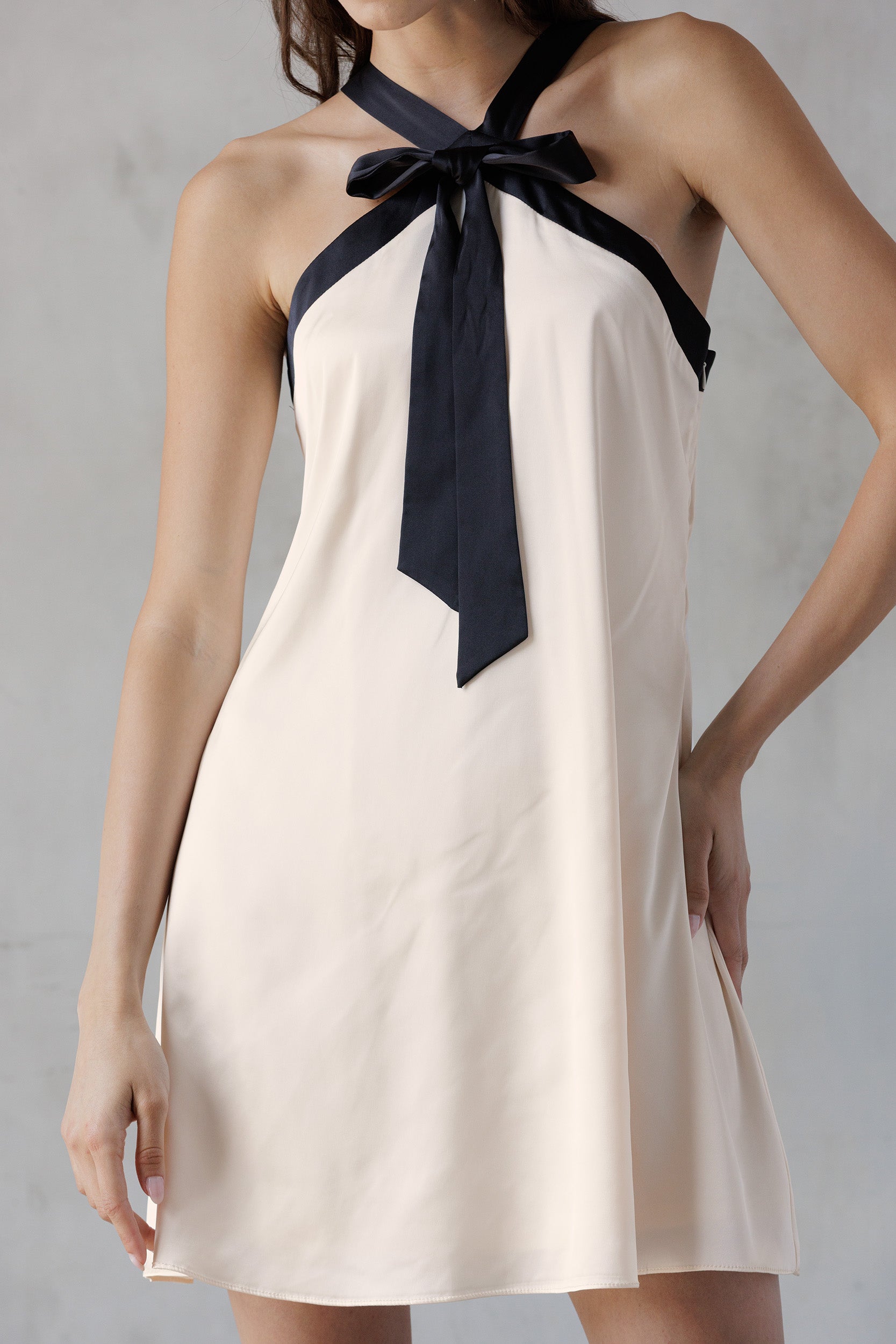 Beige halter dress with black ribbon tie on a gray background