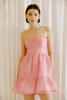 Woman wearing a pink textured dress against a white curtain background