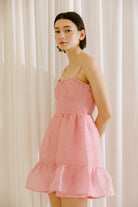 Side view of a woman wearing a pink textured dress against a white curtain background