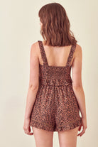 Back view of a woman wearing a leopard print cropped top and shorts on a beige background