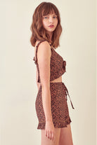 Side view of a woman wearing a leopard print cropped top and shorts on a beige background