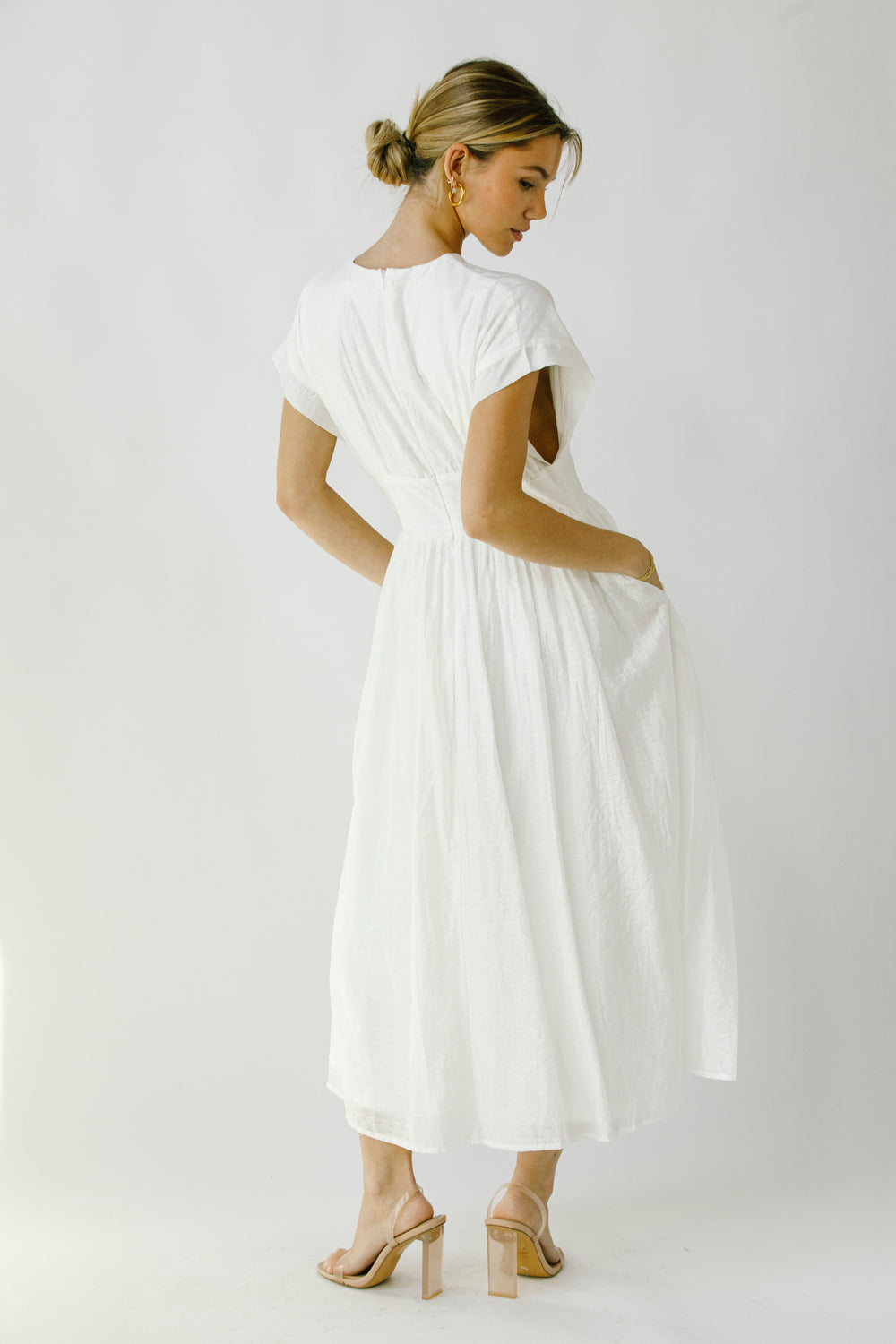 Back view of a woman wearing a white midi dress with an invisible zipper against a plain background