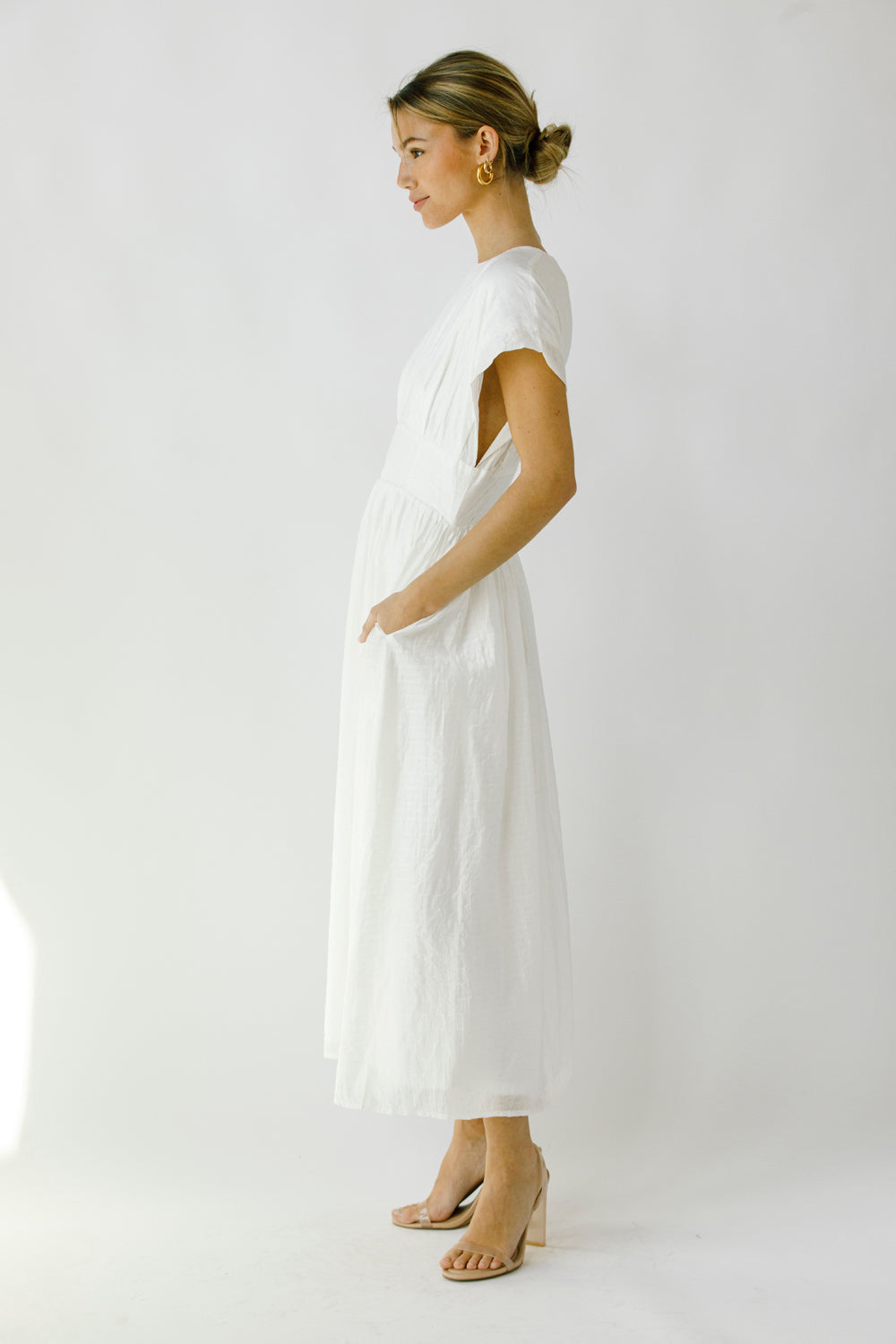 Side view of a woman wearing a white midi dress against a plain background
