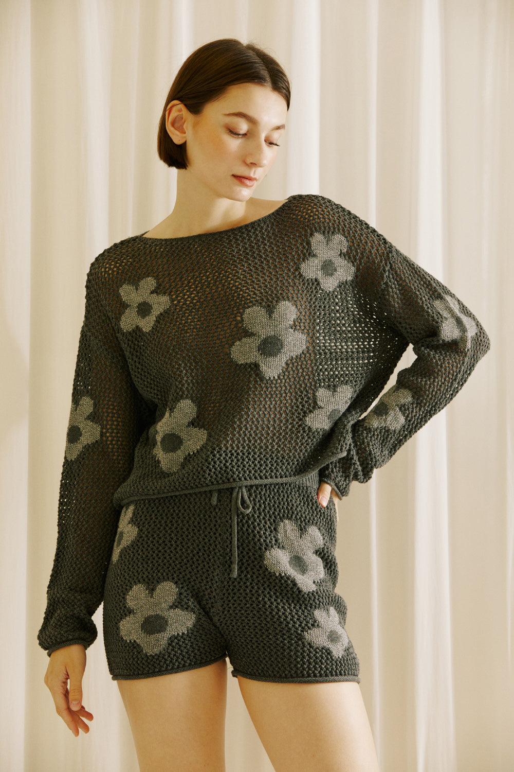 Woman wearing a dark grey crochet outfit with floral patterns against a neutral background