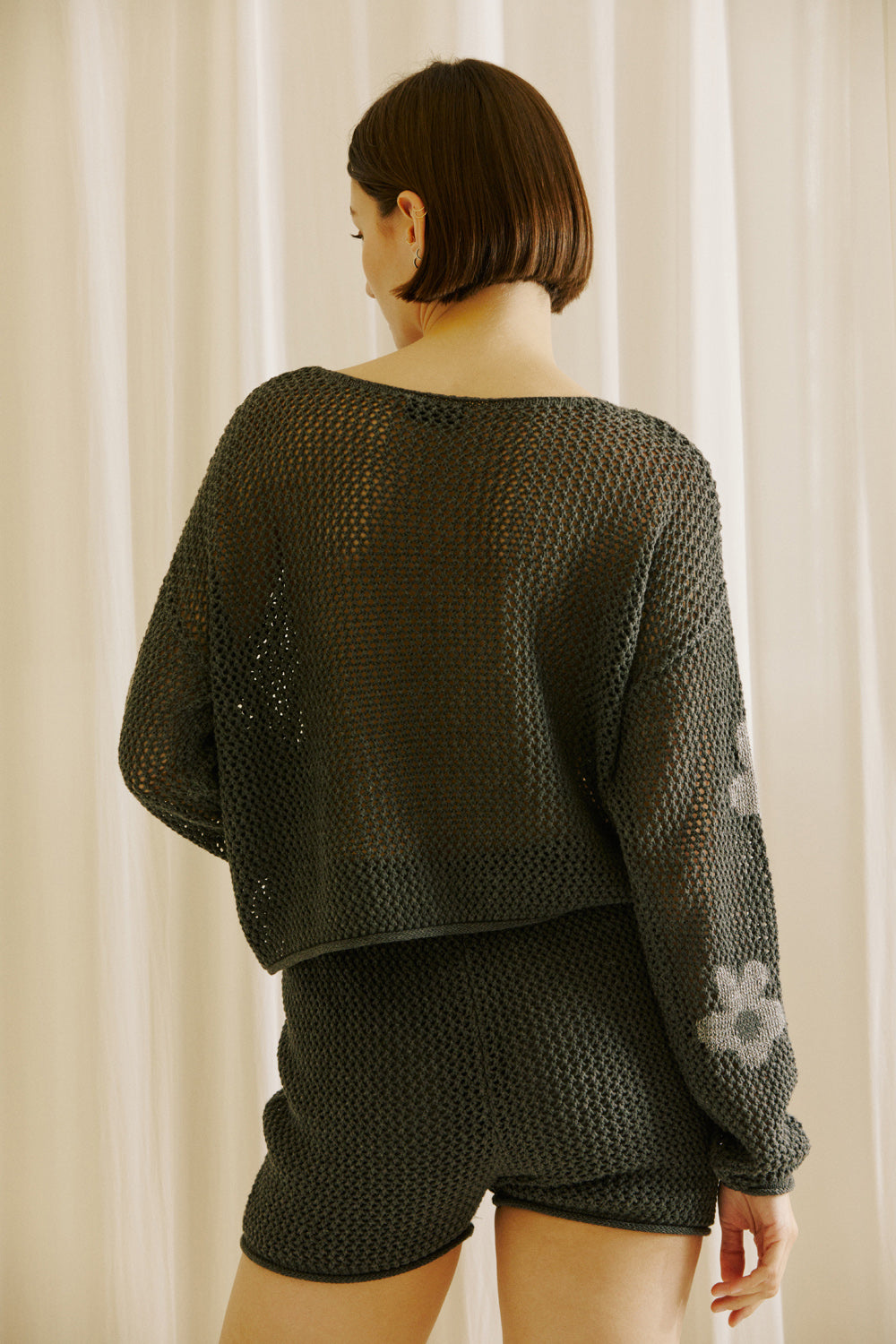 Back view of a woman wearing a dark gray knit outfit with floral patterns against a neutral background