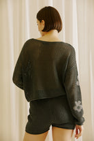 Back view of a woman wearing a dark gray knit outfit with floral patterns against a neutral background