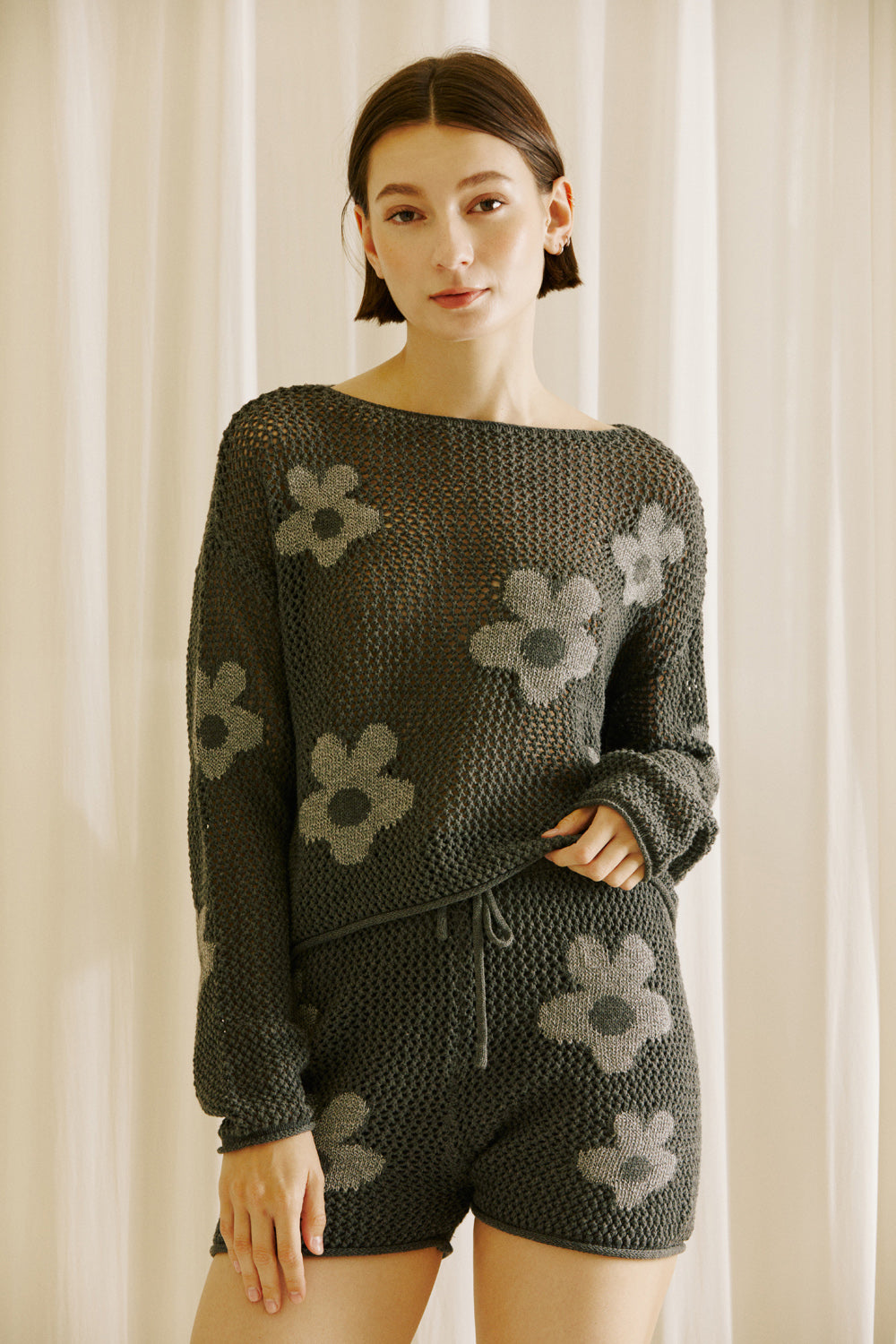 Woman wearing a dark gray knit outfit with floral patterns against a neutral background