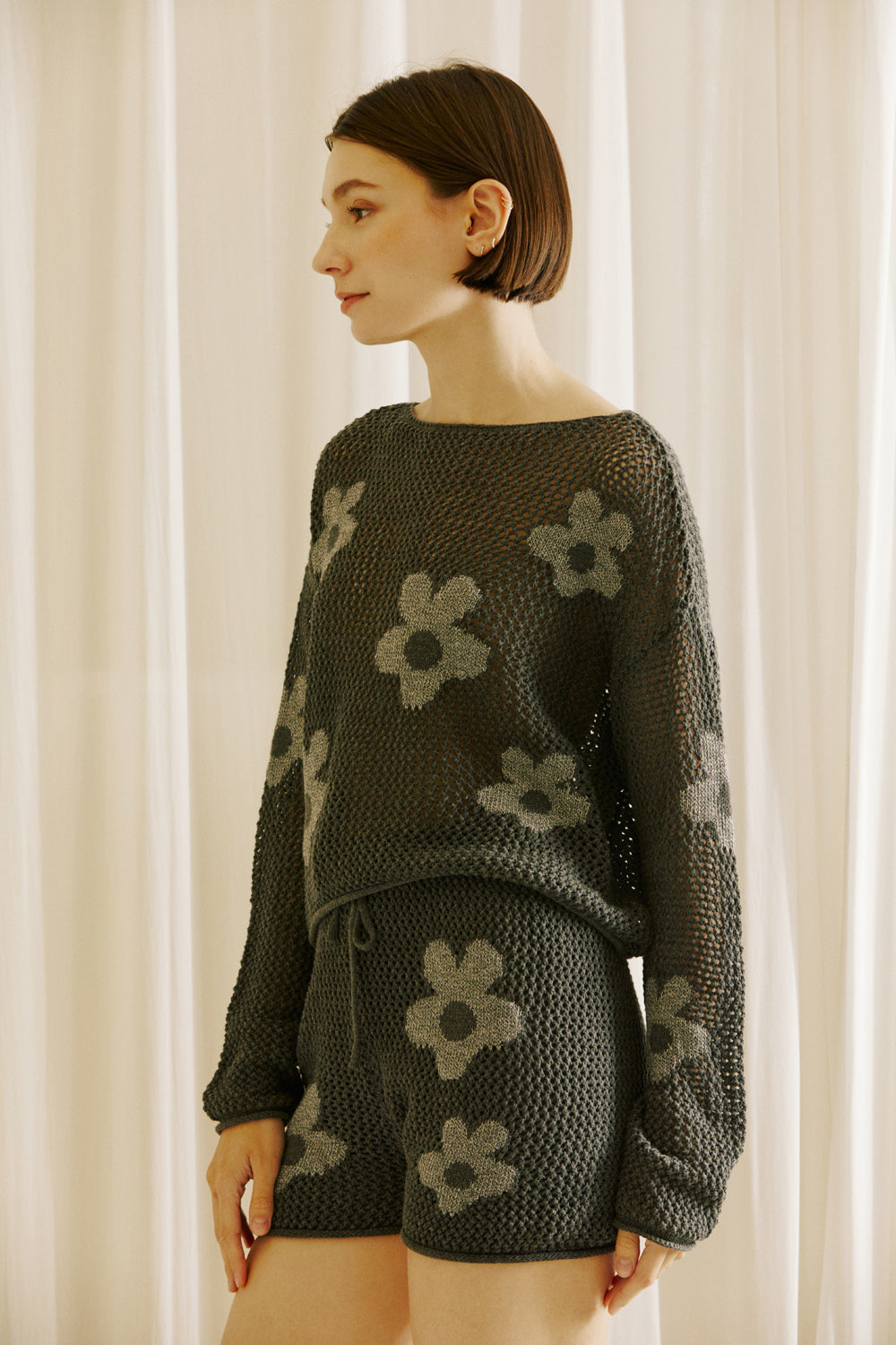 Side of a woman wearing a dark gray knit outfit with floral patterns against a neutral background