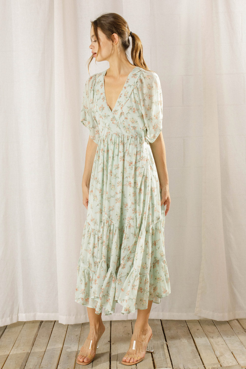 Woman wearing a light green floral dress against a white curtain background