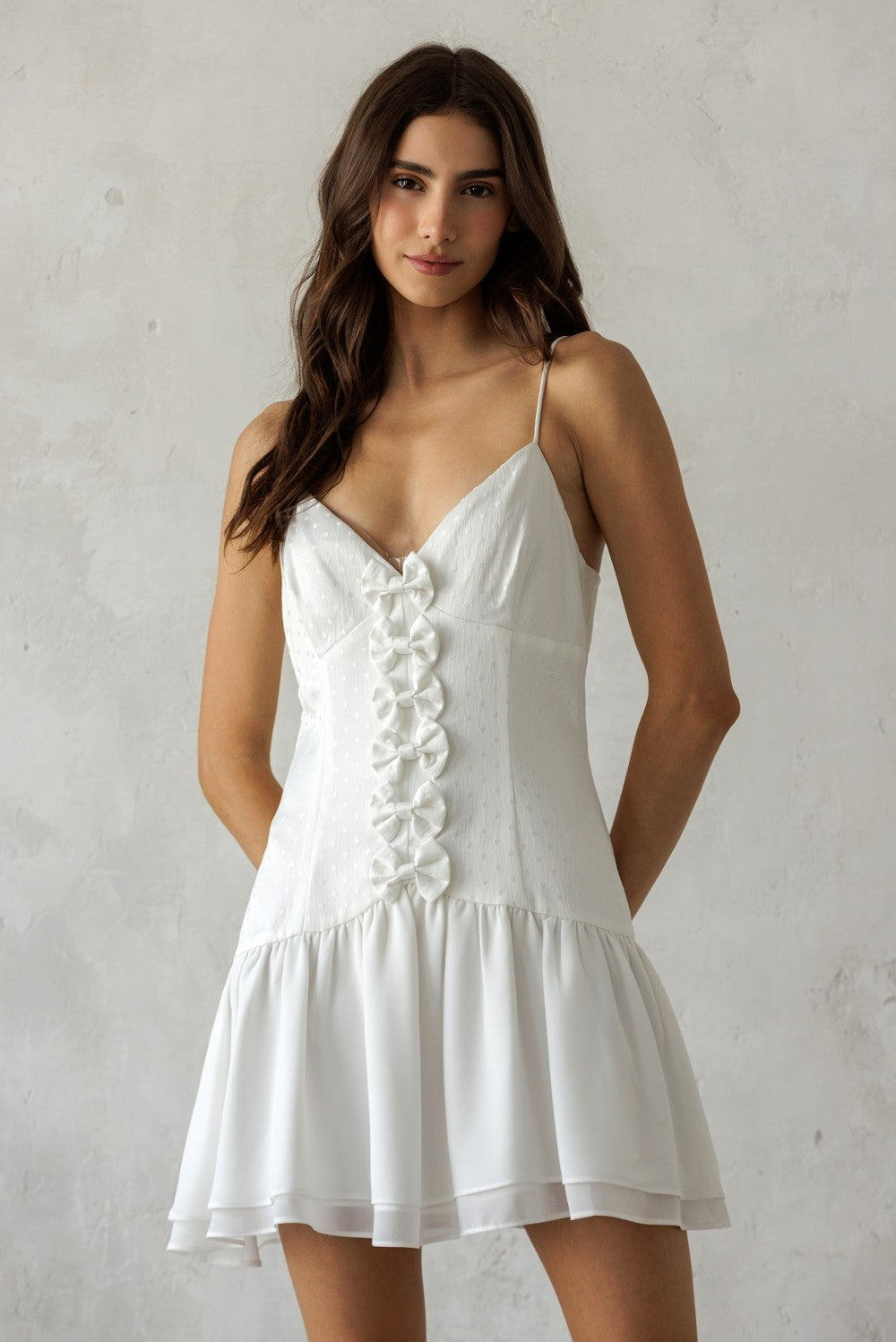 Woman wearing a white dress with bow details against a plain background