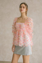 Woman wearing a pink tulle top with a blue striped skirt against a neutral wall.
