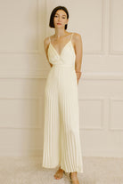 Woman wearing an ivory pleated jumpsuit against a neutral wall.