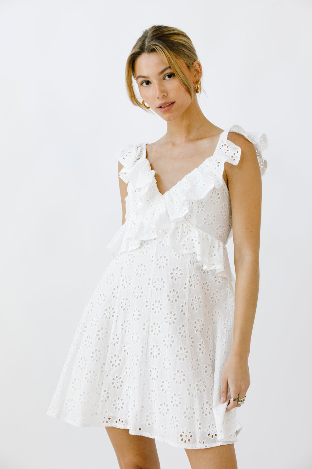 Woman wearing a white eyelet cotton mini dress on a plain background