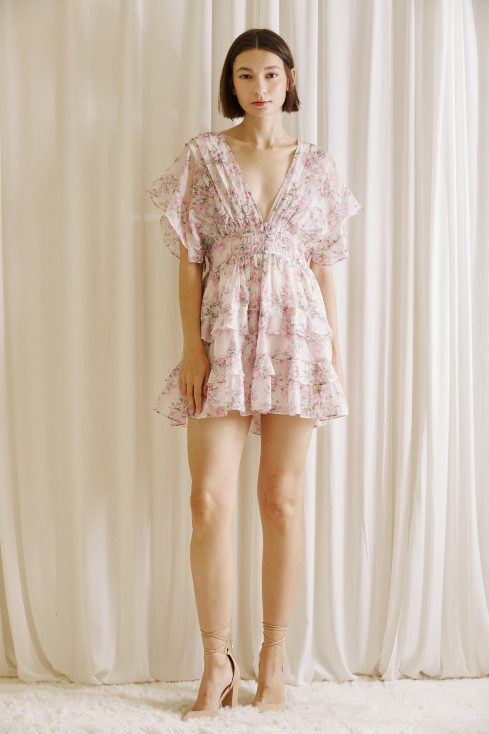 Woman wearing a pink floral dress and beige heels against a neutral background
