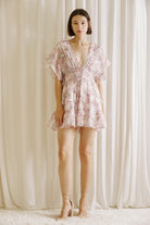 Woman wearing a pink floral dress and beige heels against a neutral background