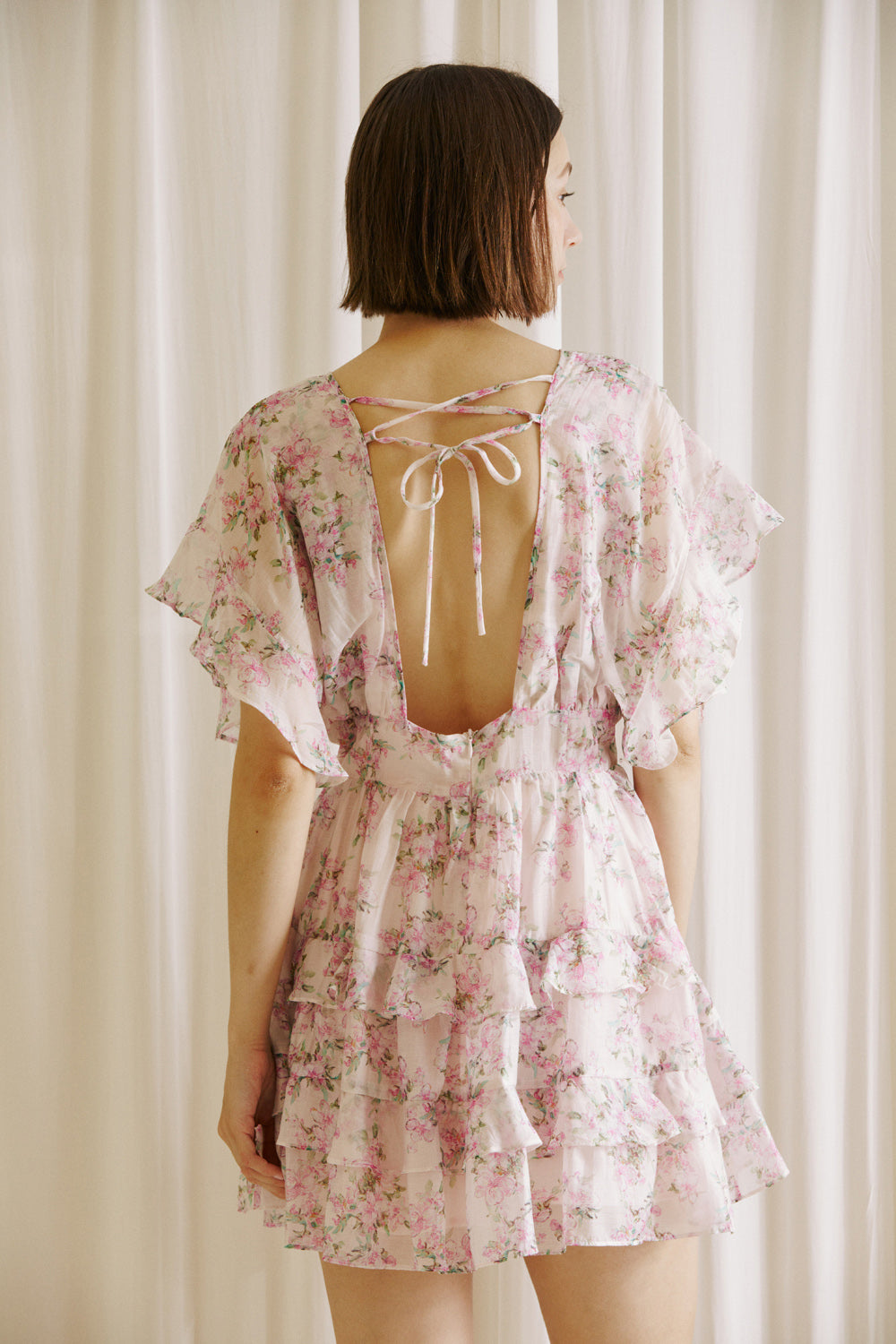 Back view of a woman wearing a pink floral dress against a neutral background